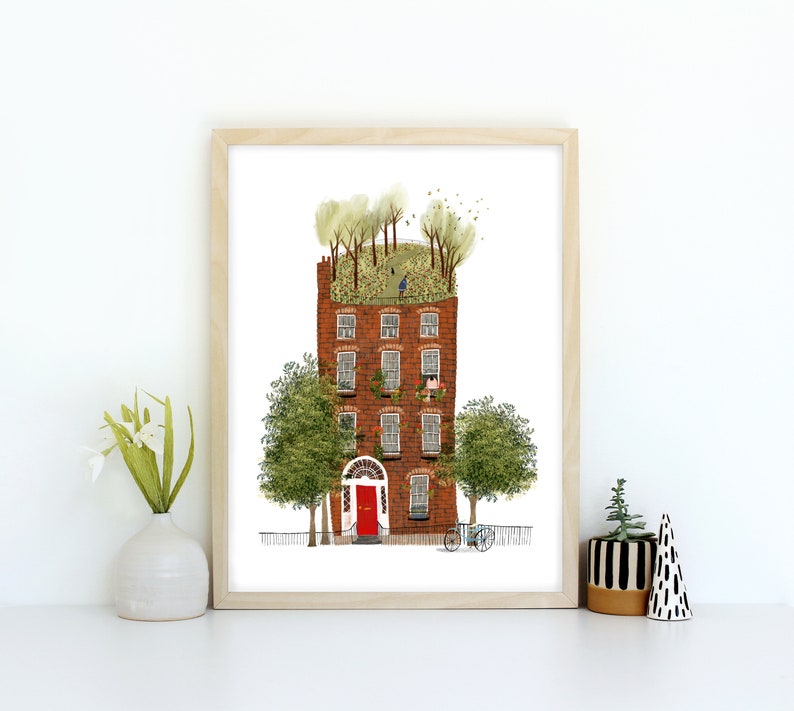 May include: A framed illustration of a red brick building with a green roof and trees growing on top. The building has windows and a red door. There are trees and a bicycle in front of the building.