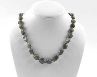 May include: A necklace made of dark green and gray labradorite stones. The stones are irregularly shaped and have a smooth, polished finish. The necklace is strung on a thin, silver-colored chain.