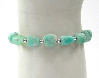 May include: A bracelet featuring polished, irregular-shaped amazonite stones in shades of green and turquoise. The stones are strung together with small silver-colored beads. The bracelet is displayed on a white surface.