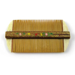 May include: A vintage comb with fine, closely spaced teeth. The comb features a decorative brown band with colorful floral and fruit designs. The handle and edges are a light beige color, and the teeth are made of thin, light brown material.