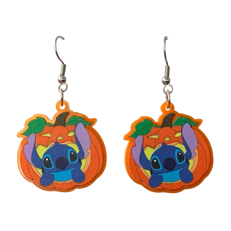 May include: A pair of orange pumpkin earrings with a blue Stitch character peeking out from the top. The earrings have silver hooks.