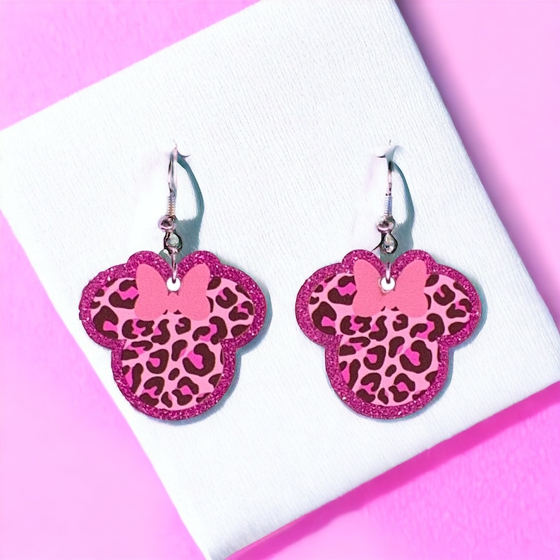 Pu&ograve; includere: Orecchini pendenti a forma di fiocco di leopardo rosa e nero. Gli orecchini sono fatti di glitter e hanno un gancio d'argento.