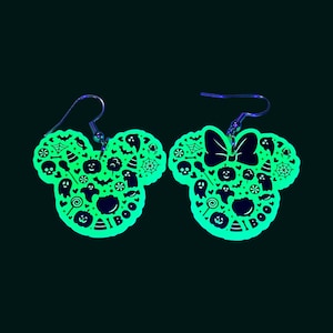 K&ouml;nnte beinhalten: Ein Paar gr&uuml;ne, im Dunkeln leuchtende Ohrringe in Form von Mickey-Maus-Ohren mit Halloween-Motiv. Die Ohrringe sind mit verschiedenen Halloween-Symbolen verziert, darunter Geister, K&uuml;rbisse, Flederm&auml;use und Mais-S&uuml;&szlig;igkeiten. Die Ohrringe haben au&szlig;erdem eine Schleife an einem Ohr und das Wort "BOO" am anderen.