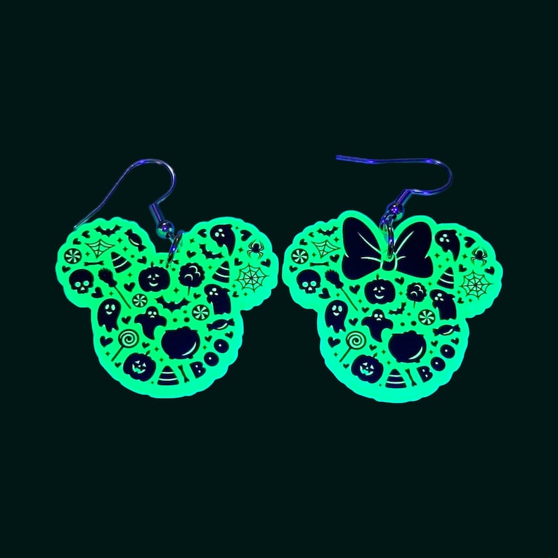 K&ouml;nnte beinhalten: Ein Paar gr&uuml;ne, im Dunkeln leuchtende Ohrringe in Form von Mickey-Maus-Ohren mit Halloween-Motiv. Die Ohrringe sind mit verschiedenen Halloween-Symbolen verziert, darunter Geister, K&uuml;rbisse, Flederm&auml;use und Mais-S&uuml;&szlig;igkeiten. Die Ohrringe haben au&szlig;erdem eine Schleife an einem Ohr und das Wort "BOO" am anderen.
