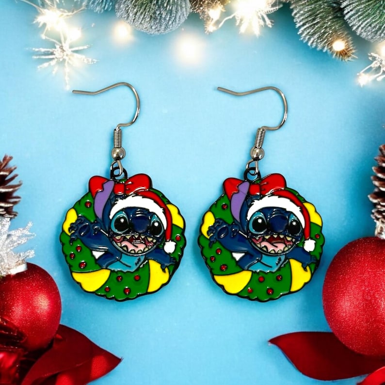 May include: A pair of blue and green Christmas-themed earrings featuring Stitch from Lilo & Stitch wearing a Santa hat and a wreath. The earrings are silver and have a hook closure.