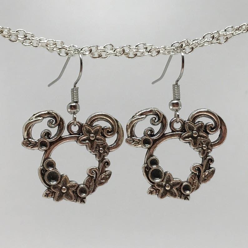May include: Silver earrings with a floral design in the shape of Mickey Mouse's head.