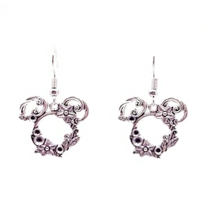 May include: Silver dangle earrings with a floral design. The earrings feature a circle with a floral pattern and a small loop at the top for hanging.