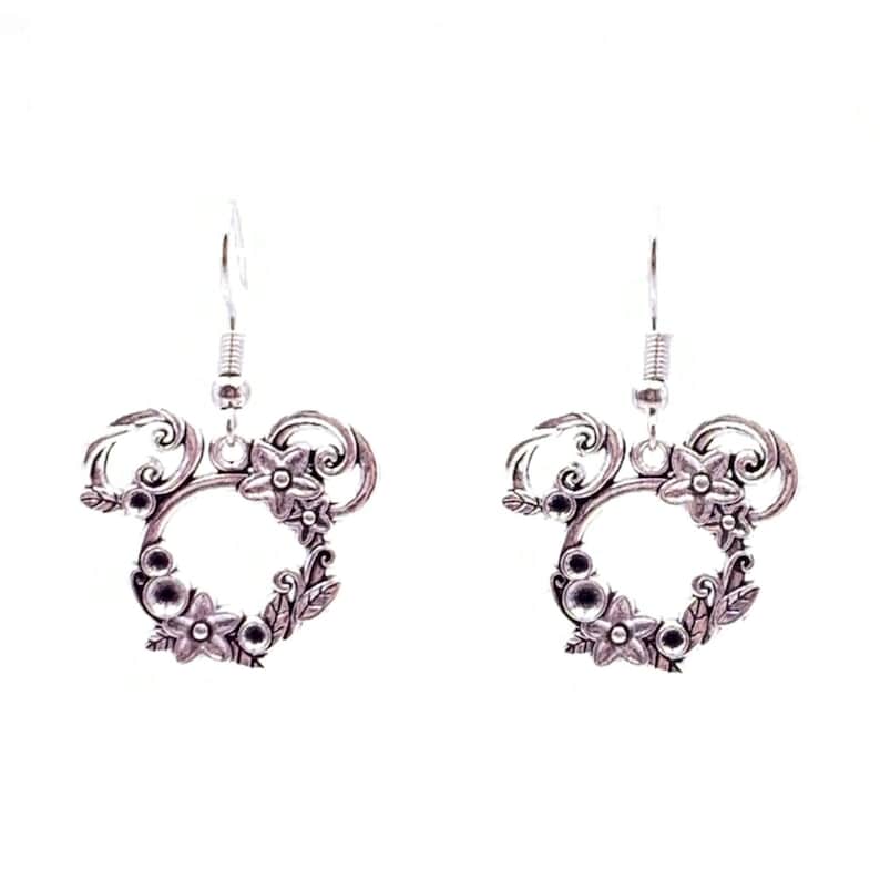 May include: Silver dangle earrings with a floral design. The earrings feature a circle with a floral pattern and a small loop at the top for hanging.