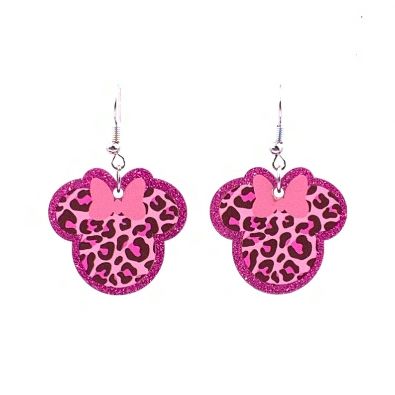 Pu&ograve; includere: Orecchini pendenti rosa e marroni con stampa leopardata e un fiocco rosa. Gli orecchini hanno la forma di una testa di topo dei cartoni animati.