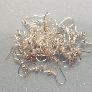May include: A pile of silver earring hooks, with a small ball at the end of each hook.