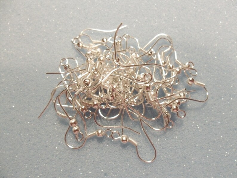 May include: A pile of silver earring hooks, with a small ball at the end of each hook.