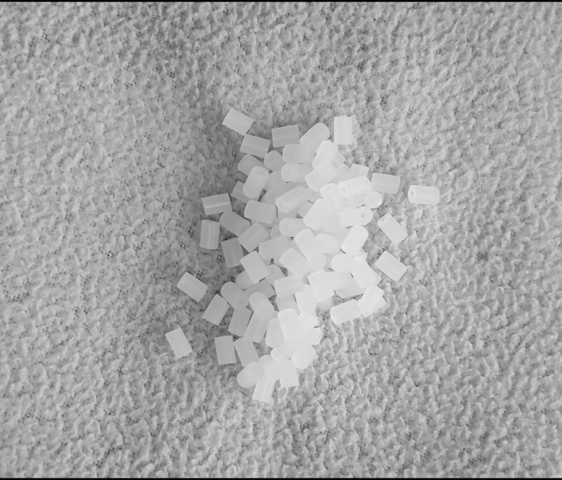 May include: A pile of small, white, plastic, cylindrical beads.