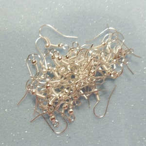 May include: A pile of silver earring hooks, with a small ball at the end of each hook.