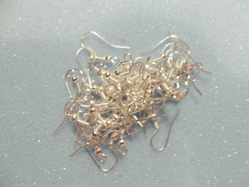 May include: A pile of silver earring hooks, with a small ball at the end of each hook.