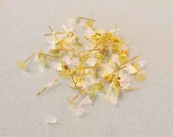 May include: A pile of gold-toned earring posts with clear plastic backs. The posts are scattered on a light blue surface.