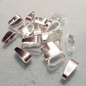 May include: A group of silver-toned metal pendant bails, used for attaching pendants to necklaces or bracelets. The bails are oval-shaped with a small loop at the top.