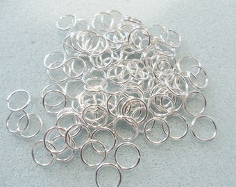May include: A large pile of silver jump rings. The rings are small and round, and they are all the same size.