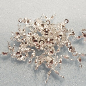 Op de afbeelding: Een stapel zilverkleurige metalen sluitingen met een afgeronde, licht gewelfde vorm. Elke sluiting heeft twee pinnen aan de ene kant en een lus aan de andere.