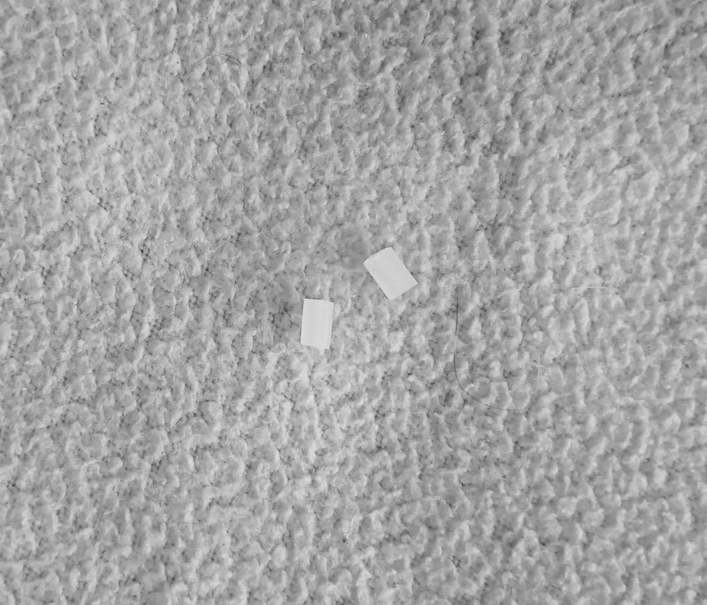 May include: Two white adhesive bandages on a gray textured surface.