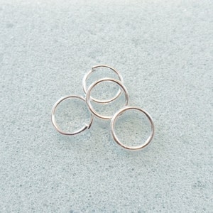 Puede incluir: Cinco anillos de salto plateados, un tipo de hallazgo de joyer&iacute;a, est&aacute;n dispuestos en una pila sobre una superficie texturizada azul claro.