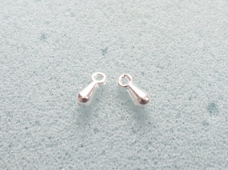 May include: Two silver teardrop-shaped charms with a loop at the top.
