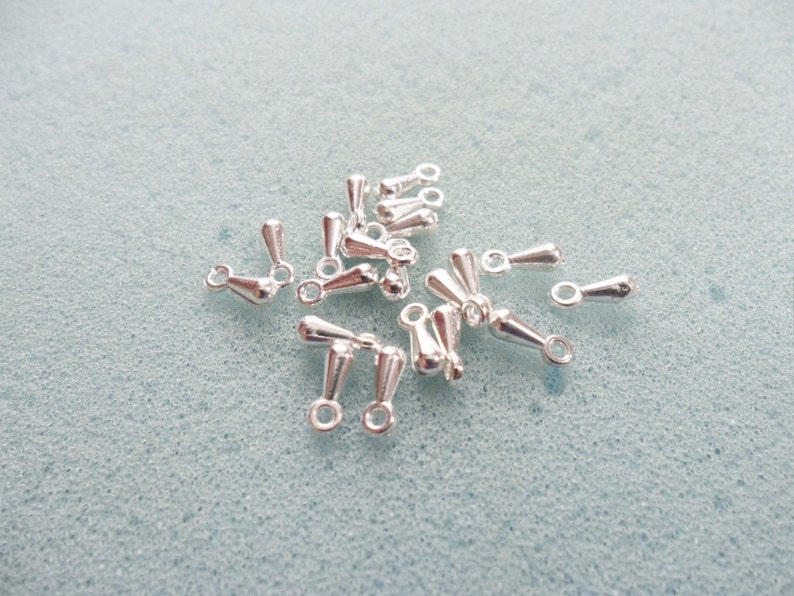 May include: A group of silver teardrop-shaped jewelry findings with a loop at the top. These findings are perfect for adding a touch of elegance to your jewelry designs.