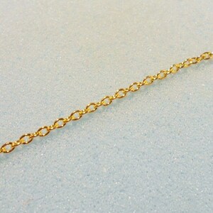Peut inclure: Un collier en cha&icirc;ne dor&eacute;e avec un design d&eacute;licat et li&eacute;. La cha&icirc;ne est pos&eacute;e &agrave; plat sur une surface bleu clair.