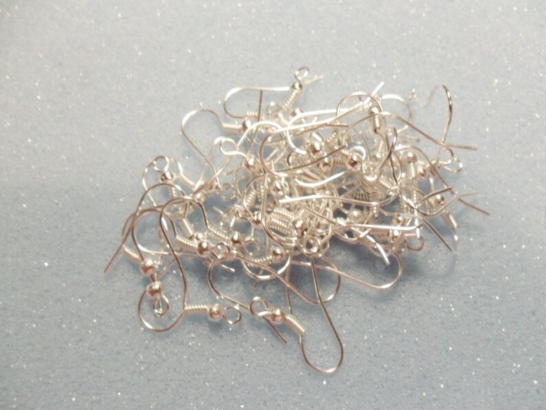 May include: A pile of silver earring hooks, a common jewelry making supply.