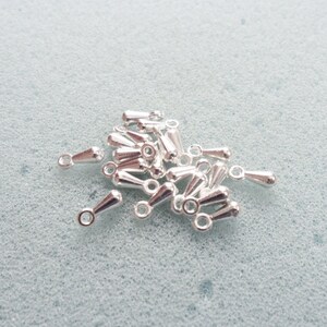 May include: A pile of silver teardrop-shaped bead caps with a loop at the top.