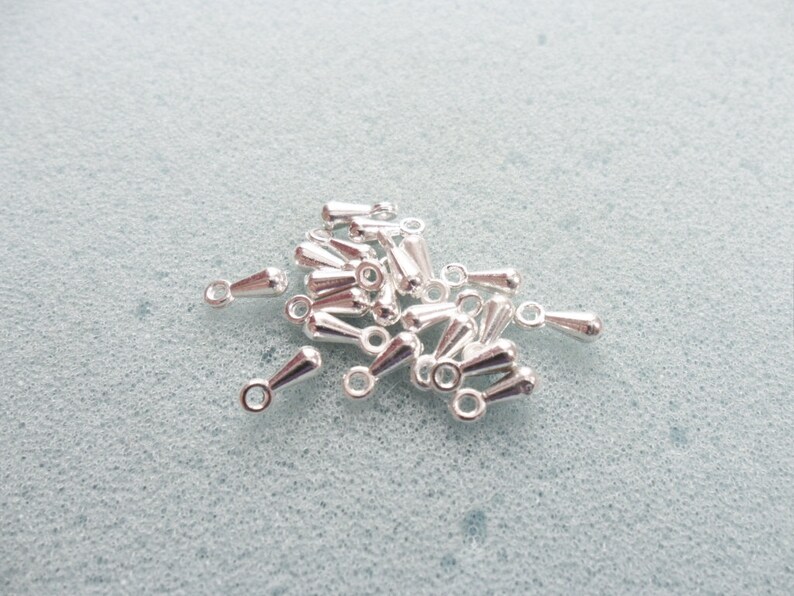 May include: A pile of silver teardrop-shaped bead caps with a loop at the top.