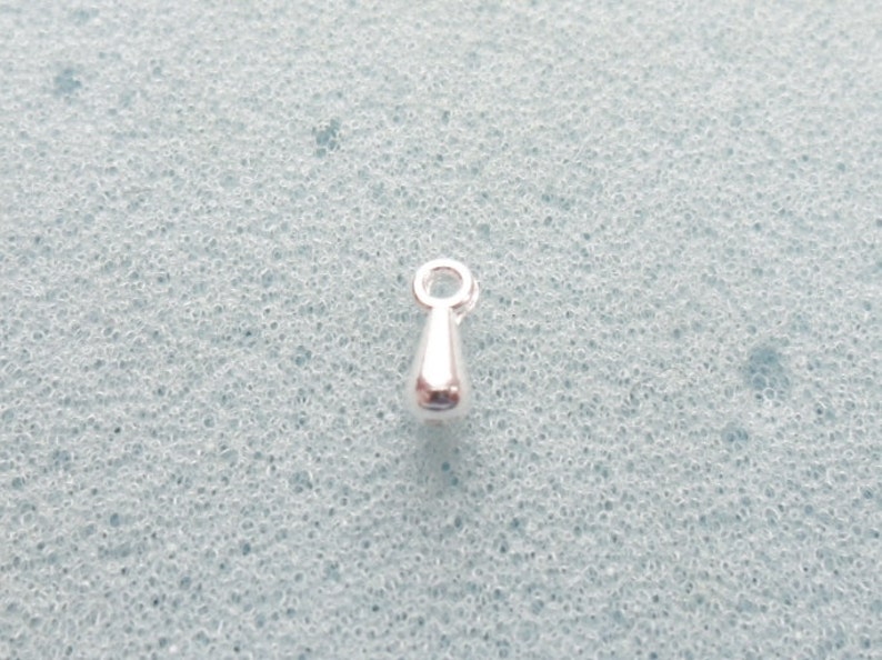 May include: A silver teardrop-shaped charm with a small loop at the top.