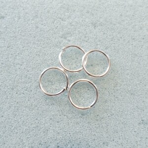 Puede incluir: Cuatro anillos de salto plateados, un tipo de hallazgo de joyer&iacute;a, est&aacute;n dispuestos sobre una superficie texturizada gris claro.
