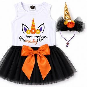 May include: A white sleeveless dress with a graphic of a unicorn face and the text Unicandy Corn, featuring a black tulle skirt with a large orange satin bow at the waist, accompanied by a matching headband with a gold unicorn horn and flowers.