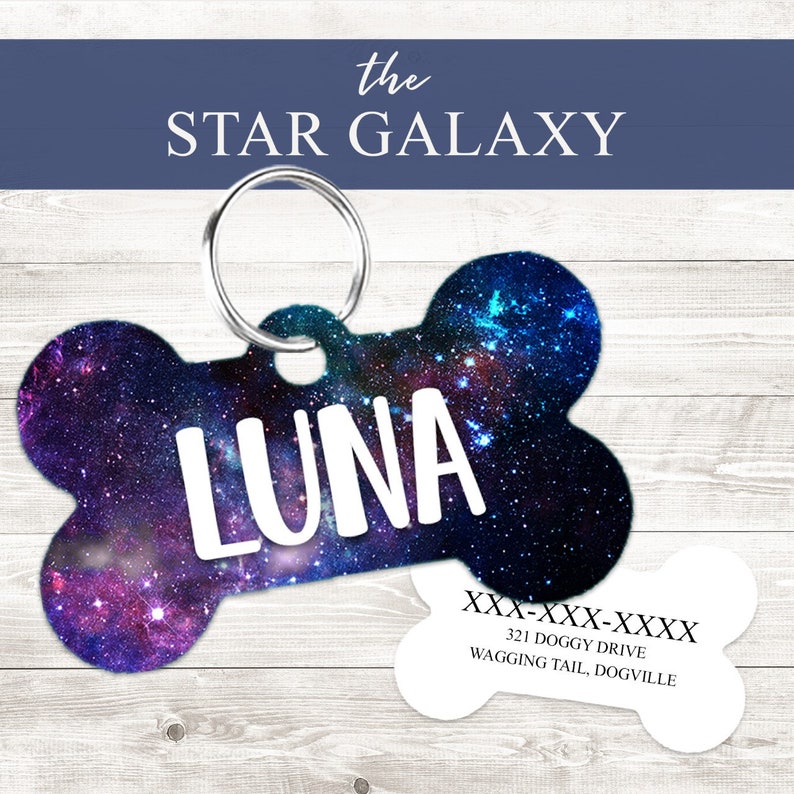 May include: A bone-shaped dog tag with a galaxy print and the name "LUNA" in white text. The tag has a silver ring for attaching to a collar. A separate white bone-shaped tag with black text includes the phone number "XXX-XXX-XXXX", the address "321 DOGGY DRIVE", and the city "WAGGING TAIL, DOGVILLE".