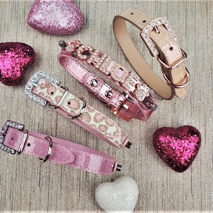 May include: Four pink dog collars with different embellishments. One collar has a leopard print, one has rhinestones spelling "CHIC", one has a rhinestone paw print, and one has a rhinestone buckle.