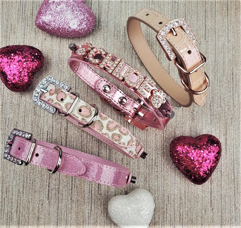 May include: Four pink dog collars with different embellishments. One collar has a leopard print, one has rhinestones spelling "CHIC", one has a rhinestone paw print, and one has a rhinestone buckle.