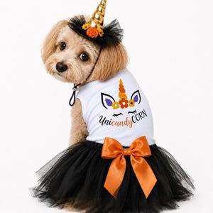 May include: A white pet tank top dress featuring a graphic of a unicorn face with orange flowers and the text Uni-candy-CORN, paired with a black tulle skirt, an orange satin bow, and a matching black tulle headband with a gold unicorn horn.