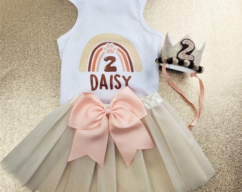 May include: A white tank top with a rainbow and paw print design, the number 2 and the name Daisy. The tank top is paired with a tulle skirt and a crown with the number 2 on it.
