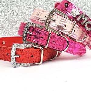 Puede incluir: Tres collares para perros en rosa, rojo y rosa claro con estampado de cuadros. Los collares tienen hebillas plateadas y están decorados con diamantes de imitación. El collar rosa tiene la palabra "MOCHI" escrita en diamantes de imitación.