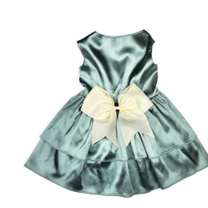 K&ouml;nnte beinhalten: Ein t&uuml;rkisfarbenes Satin-Kleid mit einer gro&szlig;en elfenbeinfarbenen Schleife auf der R&uuml;ckseite. Das Kleid hat einen mehrlagigen Rock.