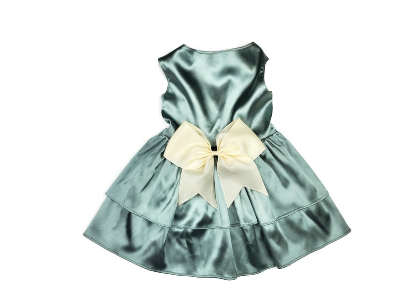 K&ouml;nnte beinhalten: Ein t&uuml;rkisfarbenes Satin-Kleid mit einer gro&szlig;en elfenbeinfarbenen Schleife auf der R&uuml;ckseite. Das Kleid hat einen mehrlagigen Rock.
