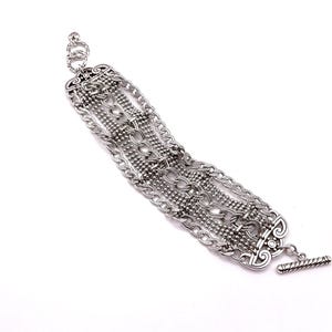 May include: Silver-toned bracelet featuring multiple chain styles and decorative elements. The bracelet has a toggle clasp and intricate detailing, showcasing a mix of chain links and beaded strands. The design is symmetrical and ornate, suitable for adding a touch of elegance.