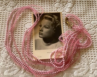 May include: A long strand of pink beaded necklace with a vintage postcard featuring a woman's portrait. The postcard reads "Mady Phi...".