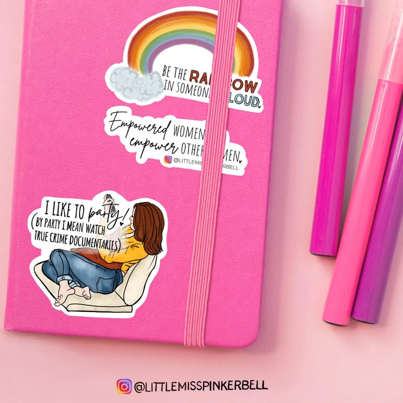 May include: Three stickers on a pink notebook. The top sticker features a rainbow with the text "Be the rainbow in someone's cloud." The middle sticker features the text "Empowered women empower other men." The bottom sticker features a cartoon illustration of a person watching true crime documentaries with the text "I like to party! (By party I mean watch true crime documentaries)".