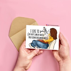 May include: A white card with a cartoon illustration of a person sitting on a couch and watching TV. The text on the card reads "I like to party! (By party I mean watch true crime documentaries)"