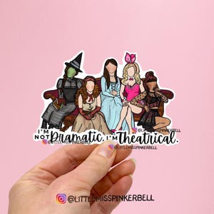 May include: A sticker featuring a group of cartoon women in various costumes, seated on a brown couch. The text reads "I'm not dramatic, I'm theatrical." The background is pink.