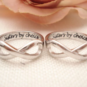 May include: Two silver infinity rings with the inscription "Sisters by choice" on each band.