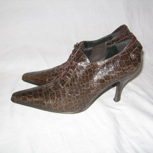 以下が含まれることがあります： クロコダイル柄のレースアップディテールが付いた、ブラウンの革製のヒールシューズです。