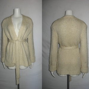 May include: A cream-colored knitted cardigan with a long tie belt. The cardigan has a V-neck and long sleeves.