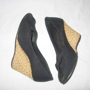 May include: Pair of black wedge sandals with woven jute heels. The sandals have a closed-toe design and a fabric upper. The wedge heels provide a comfortable lift. These shoes are suitable for casual or semi-formal occasions.